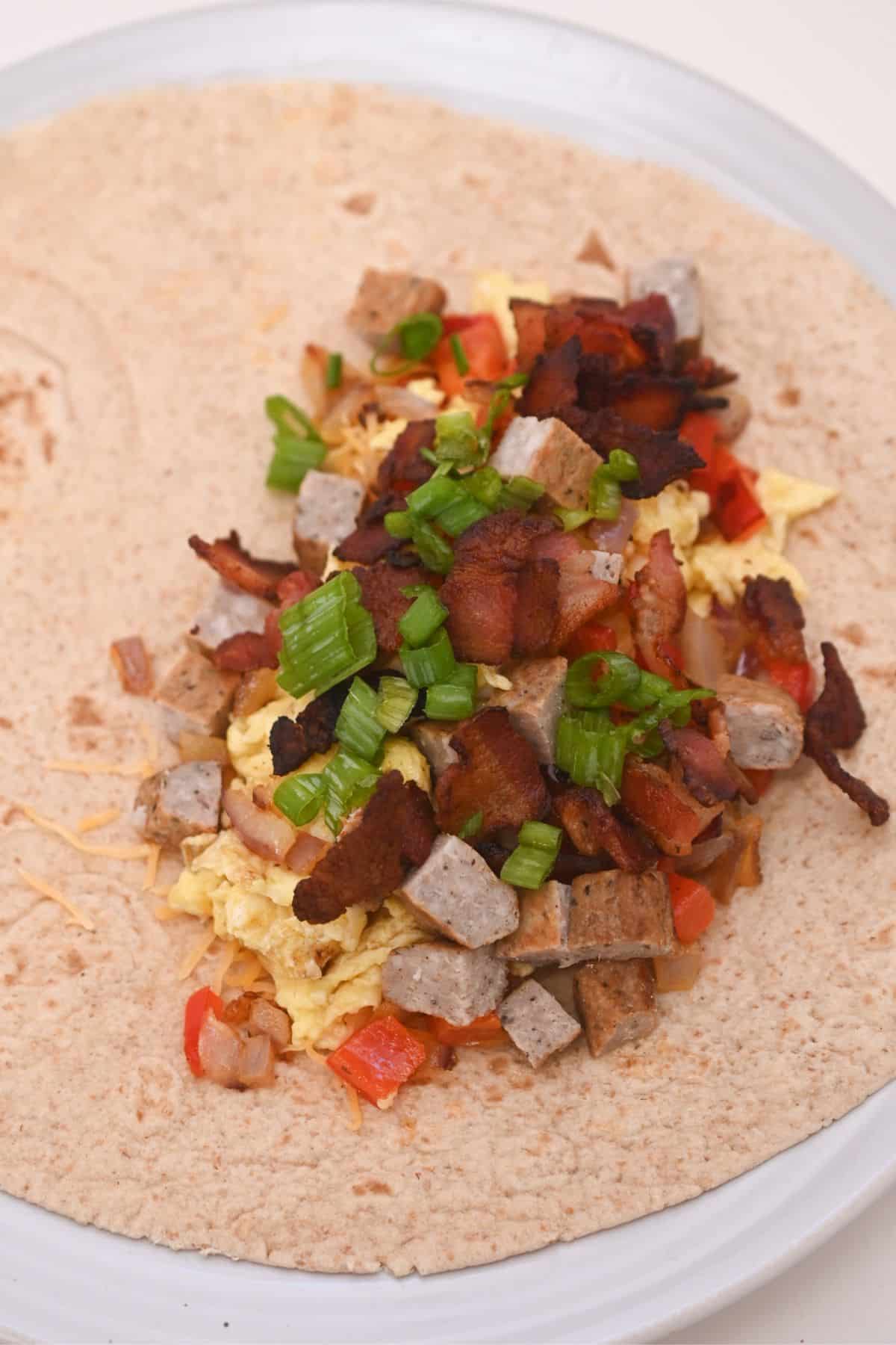 cheese, eggs, vegetables, sausage, bacon and green onions in tortilla